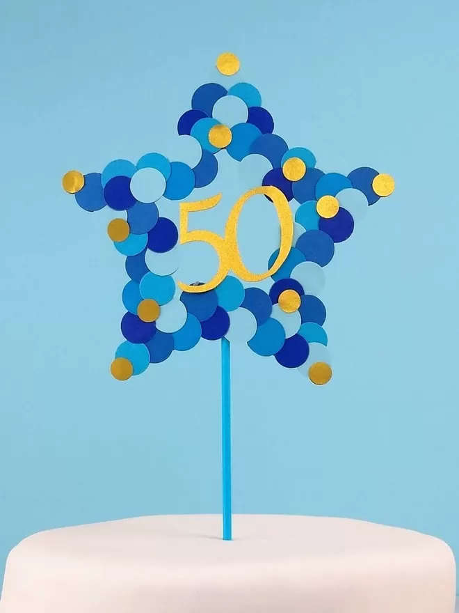 Star shaped cake topper in mixed blues with gold dots. Number 50 is displayed in gold in the centre of the star
