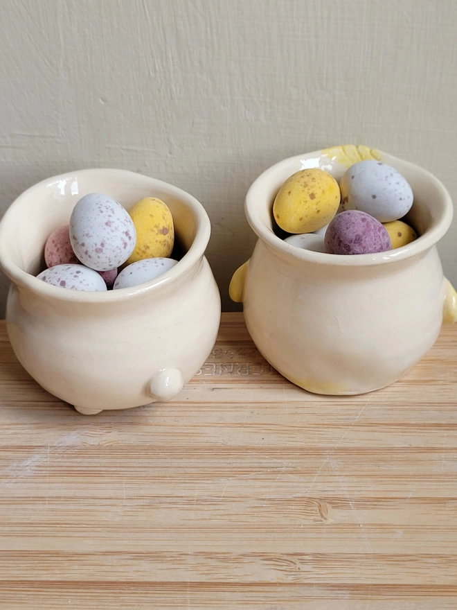 the back view of two ceramic egg cups both with mini chocolate Easter eggs in and one had a bunny tail the other chick wings on 