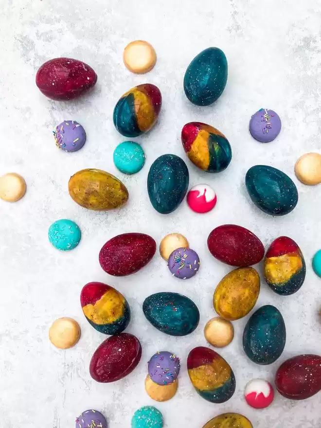 colourful easter eggs scattered amongst mini macarons on a white surface