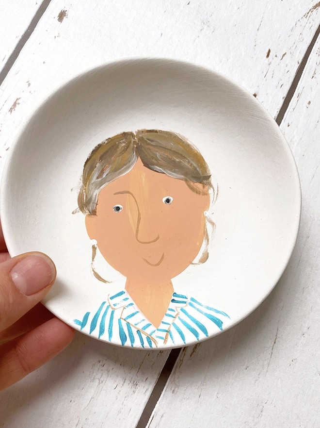 small white plate with stylised painted portrait of girl with striped blue and white shirt