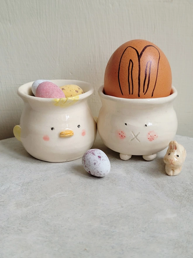 Easter bunny and chick pottery egg cup with an egg in the bunny cup with ears drawn on it and mini chocolate eggs in the chick egg cup