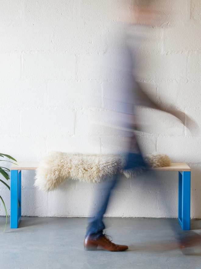 motion bluyr of a man in blue jeans walking past a minimalist bench with chunky blue legs