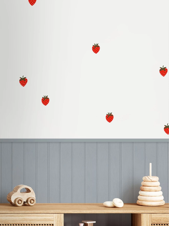 Strawberry wall stickers in playroom with blue grey wall panelling and wooden toys close up