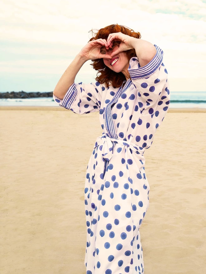 Red haired girl wearing block printed soft white and navy spot robe on the beach