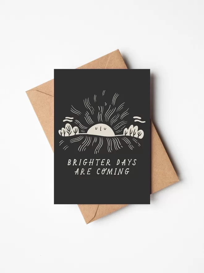 Black and white friendship card with illustration and the words brighter days are coming written on it with a brown envelope underneath it