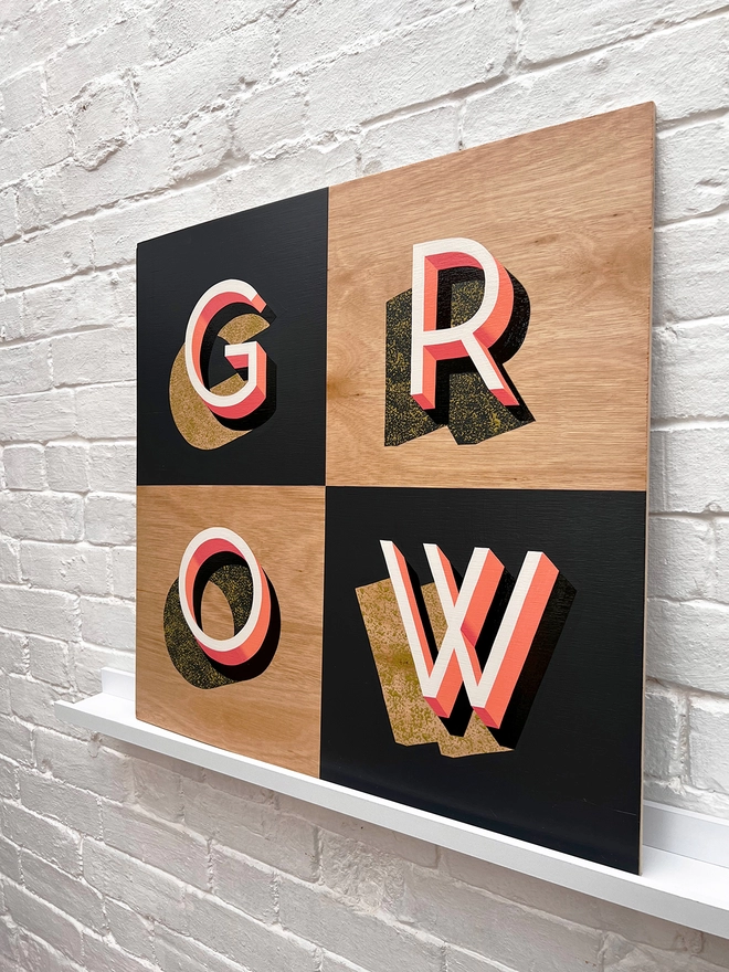 GROW hand painted sign in coral, dark grey and chartreuse, against a white brick wall, at an angle. 