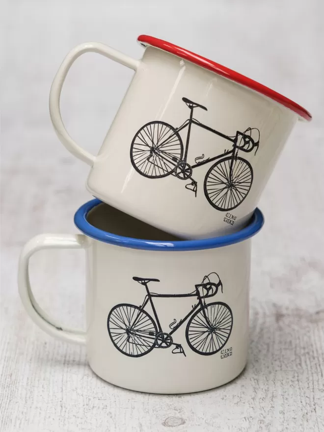 Picture of 2 Cream Enamel Mugs with a bicycle design etched onto it, taken from an original Lino Print. 1 has a blue rim, and the other has a red rim.