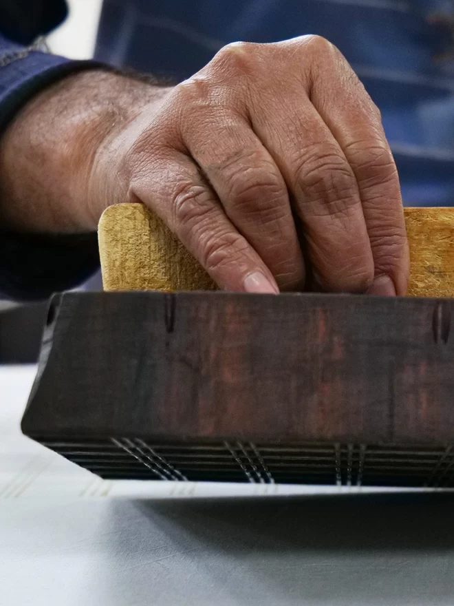 hands holding a wooden block to print a patten onto fabric 