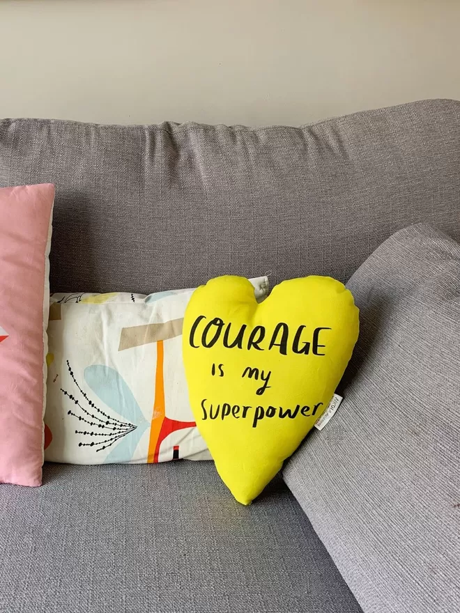 Courage heart plushie in yellow seen on a sofa