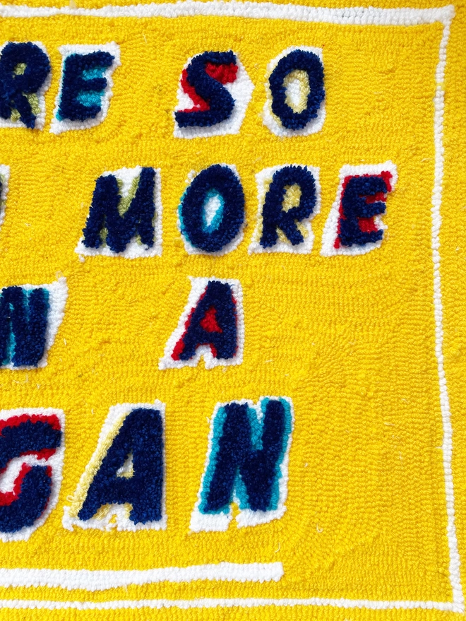 close up of blue tufted lettering on a yellow wool background with white underlines and edging frame
