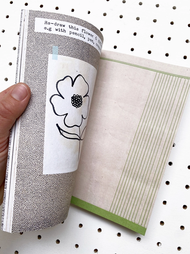 open book with instructions, flower drawing and aged paper pages on white pegboard 
