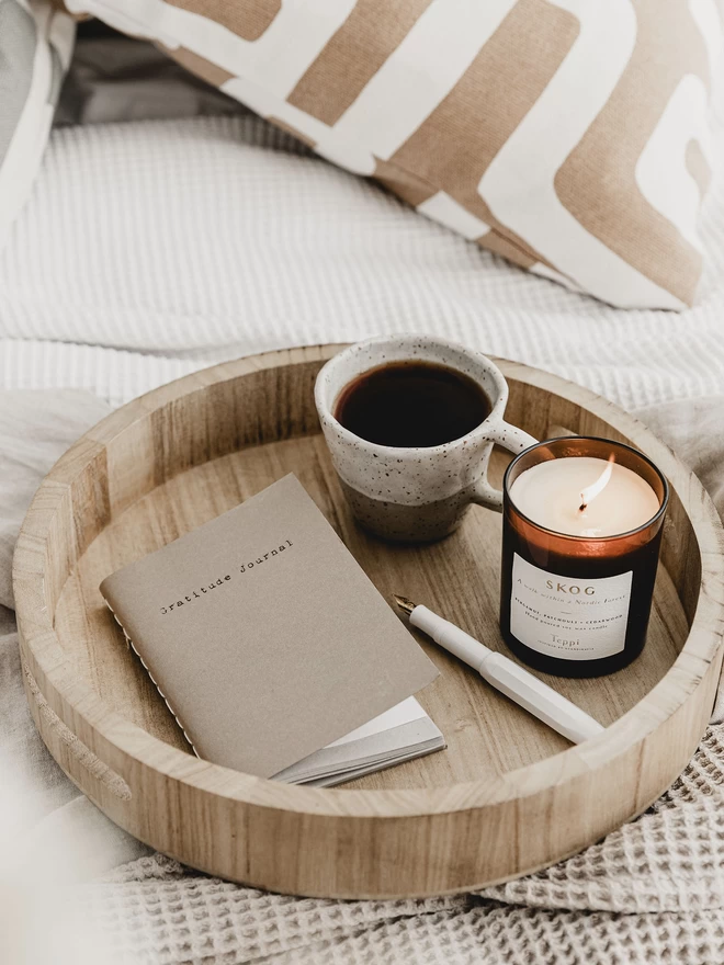 wooden tray holding a a6 gratitude journal, a mug of coffee and a lit candle