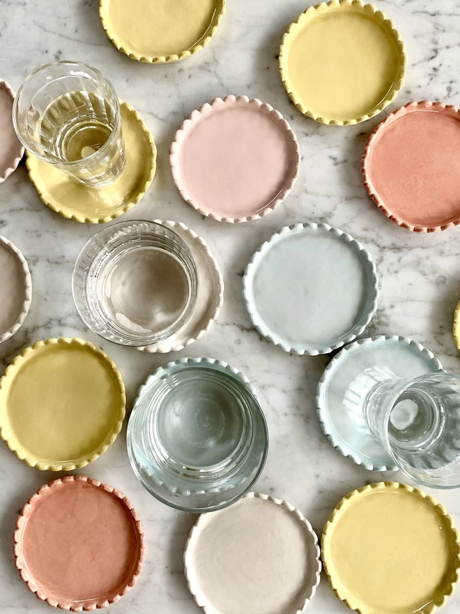 a large group of scalloped edge coasters in pastel shades with water glasses
