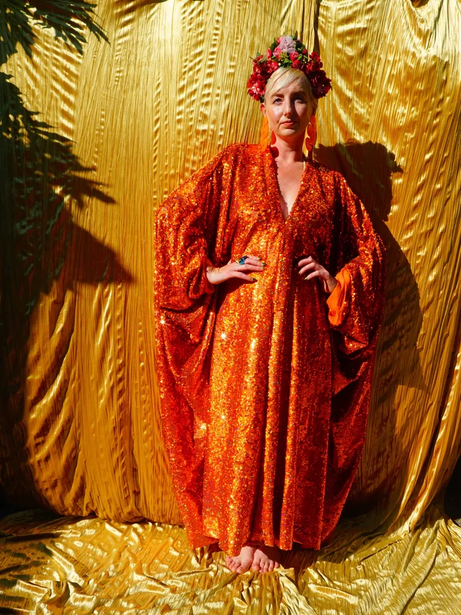 Woman seen wearing the orange v-neck sequin kaftan by fumbalina seen from the front.