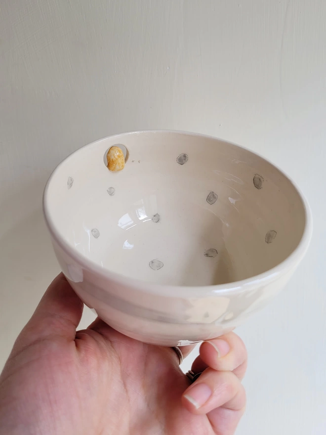 spotty grey and off white pottery bowl held in a hand with a cut out hole showing the back of a barn owl perching
