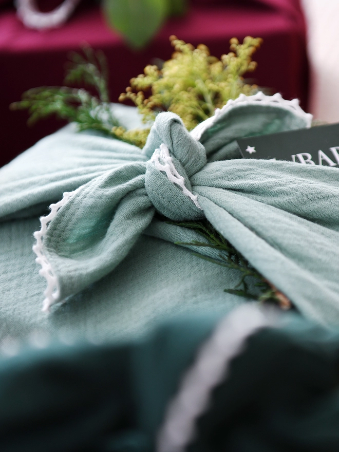 A gift wrapped in a cotton fabric wrap has yellow flowers tucked into the knot.