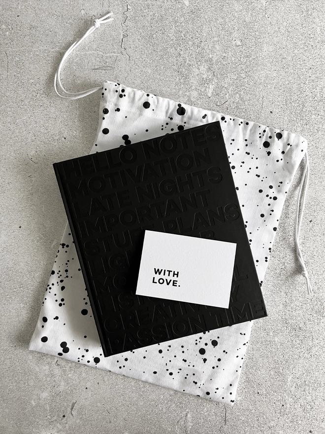 Dust bag with planner laid on top with a "with love" notecard laid on the black planner.