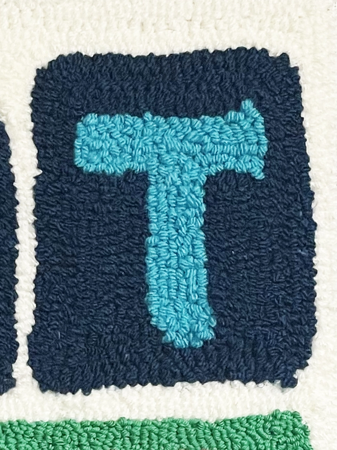 Large cyan tufted wool "T" on a navy wool background