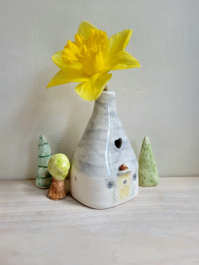 3 ceramic trees of different styles situated around a pottery bud vase with a yellow daffodil inside 