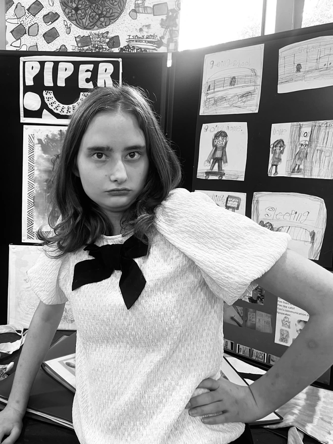 Black and White photo of Piper who is looking at the camera with had on her hip in front of her work displayed