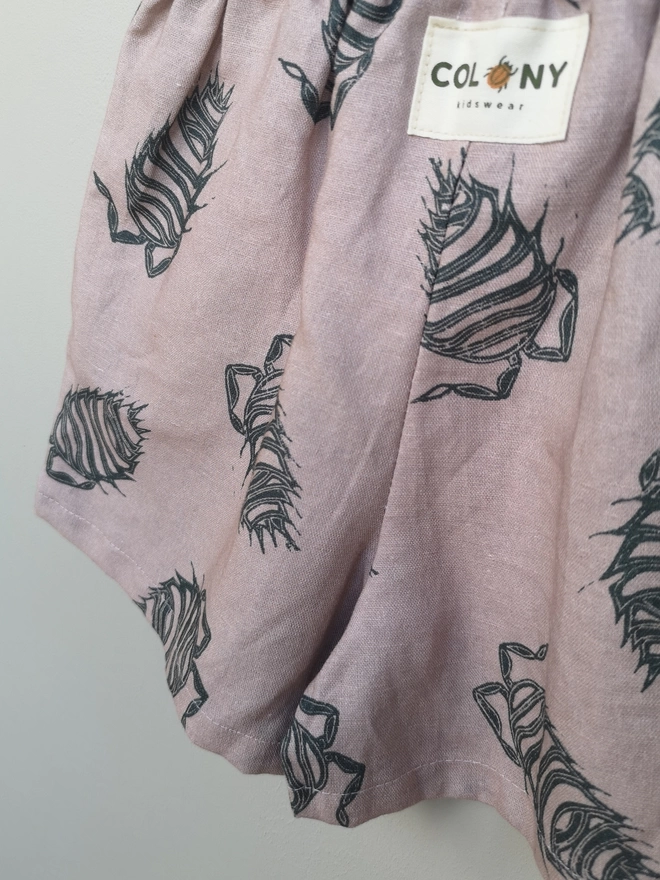 Pink cotton linen lightweight unisex childrens shorts. Featuring a delicate grey woodlouse print. Simple design with elasticated waist and side seam pockets. 