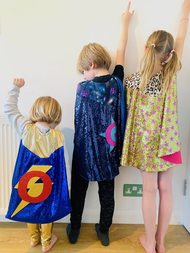 Three children wearing the hero capes. Each cape has a different colour combination.
