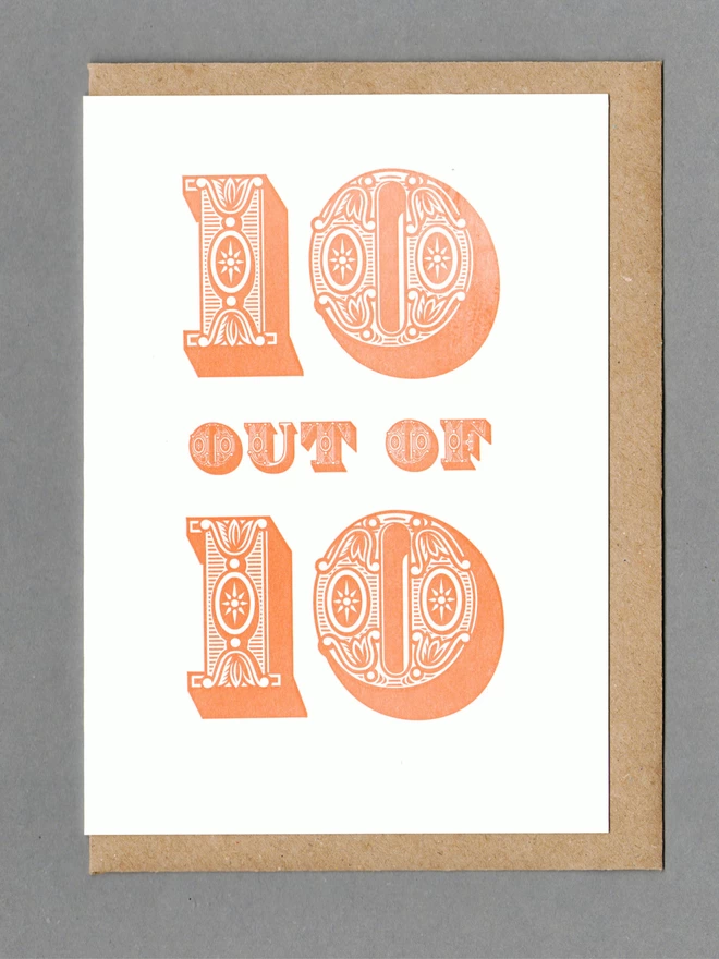 White card with orange text reading '10 OUT OF 10' with a kraft envelope behind it