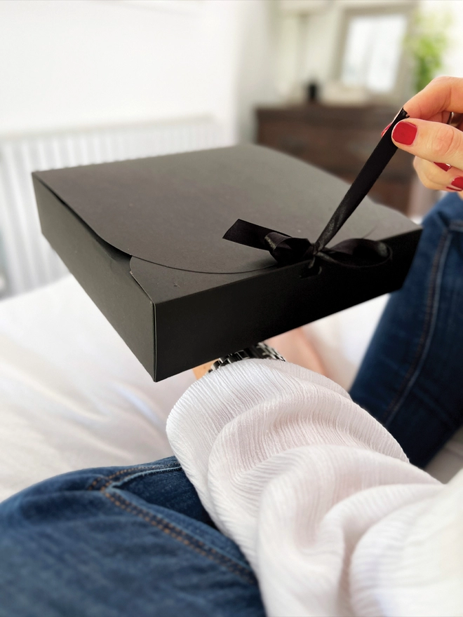Lady undoing a bow on a black gift box. 