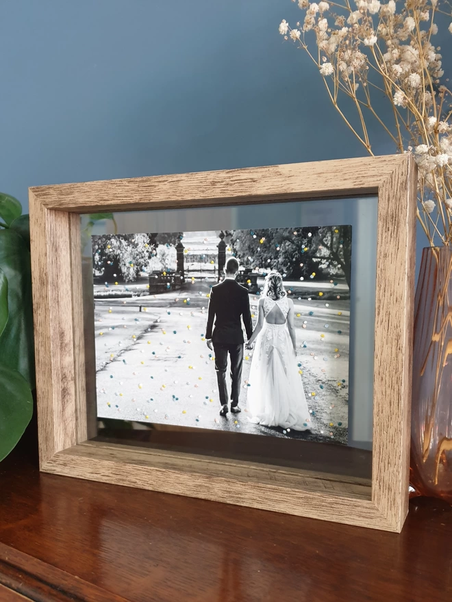 Wedding photo with hand embroidered confetti framed in double glass frame on desk