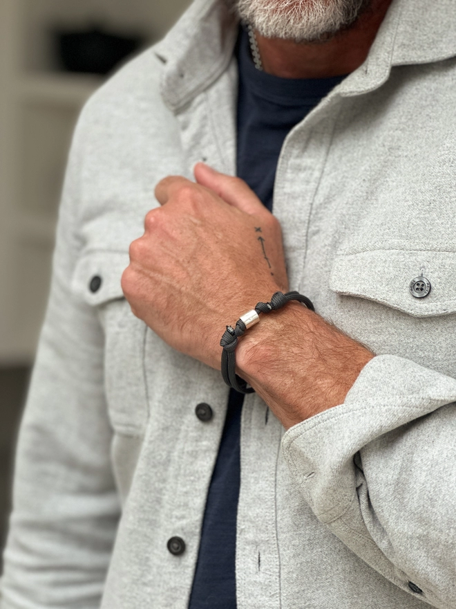 model wears personalised sterling silver men's bracelet on grey cord