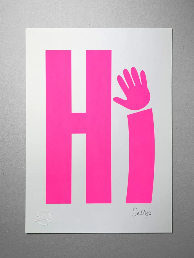 An A3 piece of paper sits on a grey background, with a neon pink screenprinted Hi - the i is a waving hand - the Salty’s signature is in the bottom right corner.