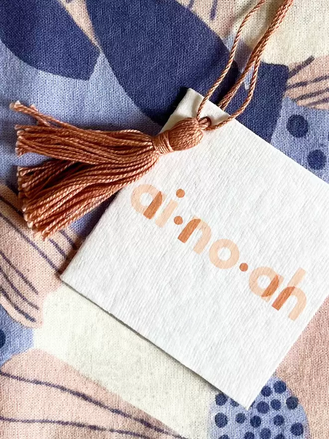 Detail of ainoah recycled swing tag showing the brand logo with tassel hanging loop