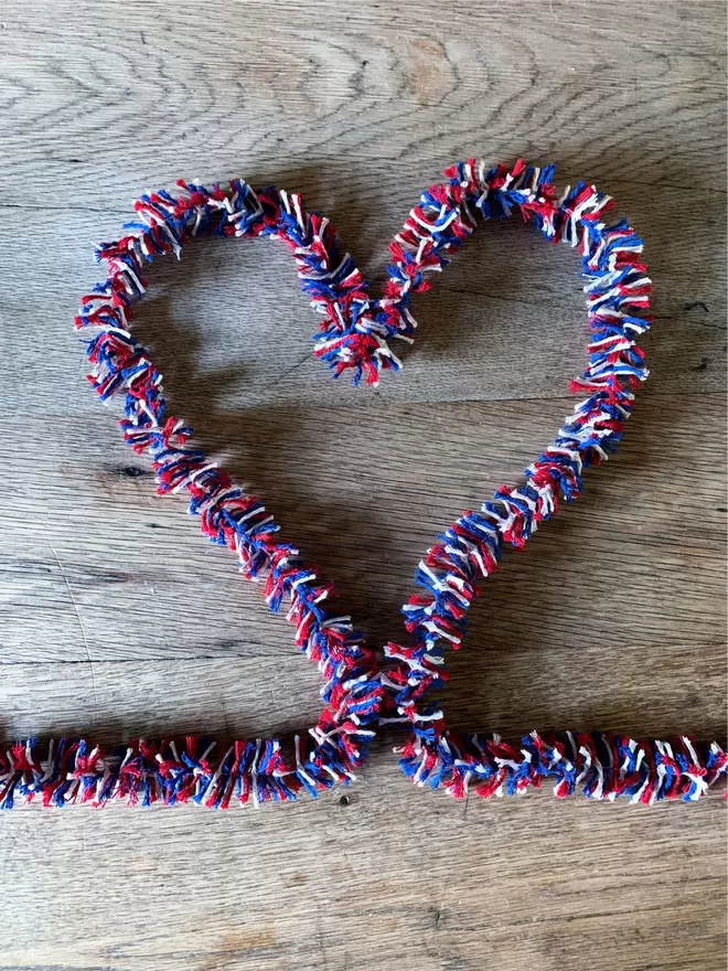 Red white and blue string tinsel shaped to form a heart on an oak table