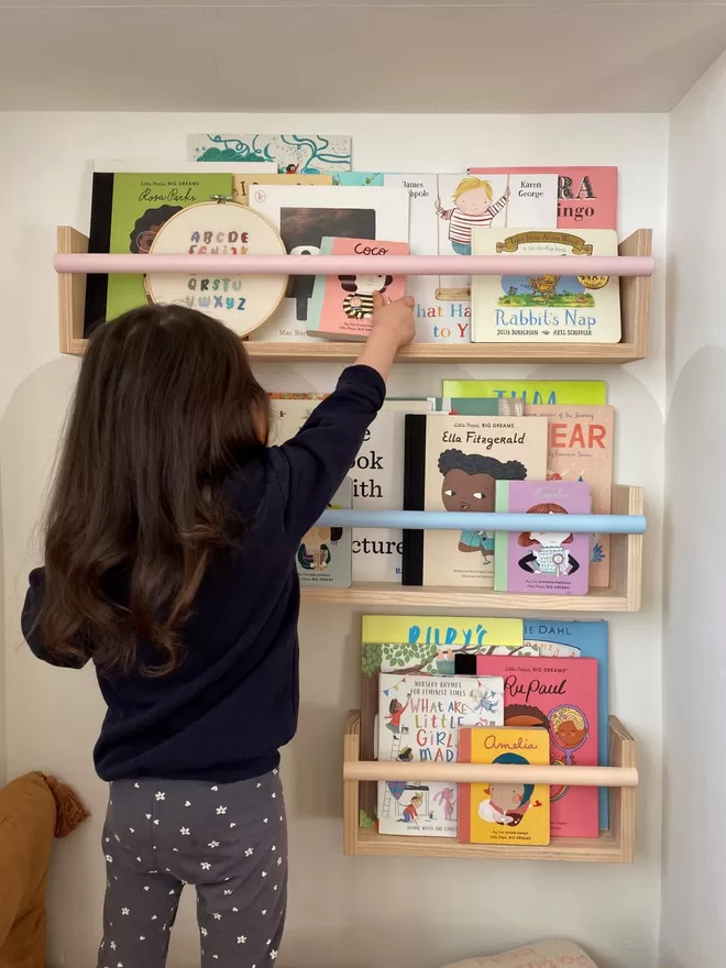 The Flip-It Shelf seen filled with books and a child reaching up to get a book from the shelf.