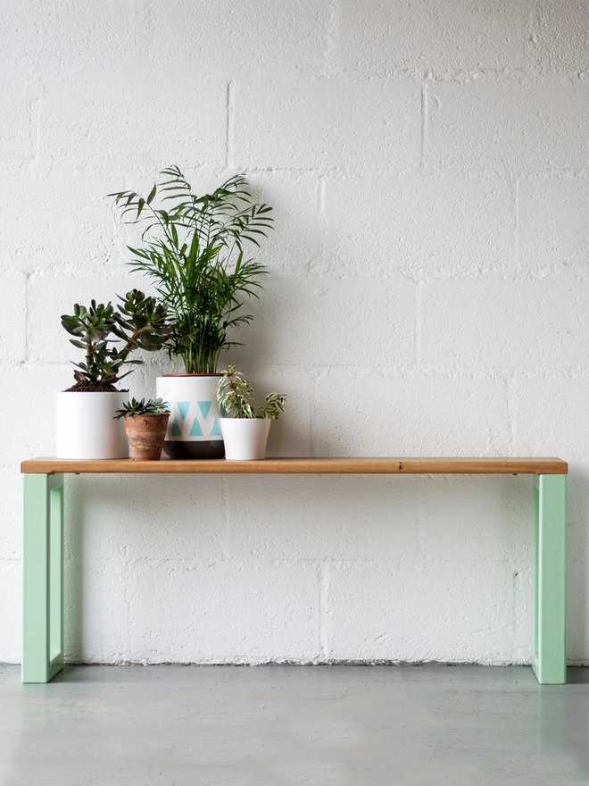 oak bench with chunky box section steel legs in pistachio green, set against a hallway wall with pot plants at one end.