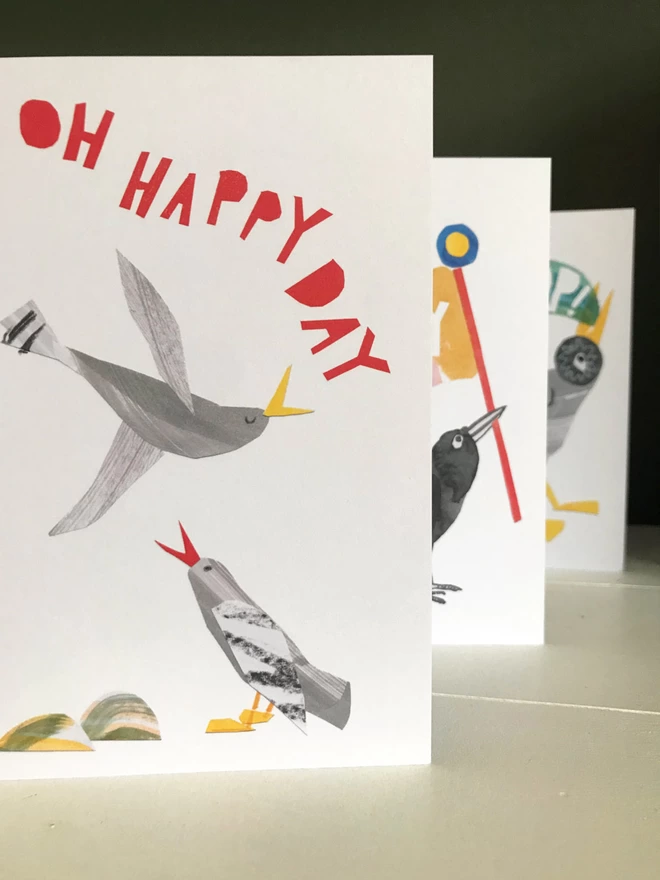 Set of three illustrated greetings cards by Esther Kent showing colourful lettering and stylised birds. The front card that reads 'Oh Happy Day' in red.