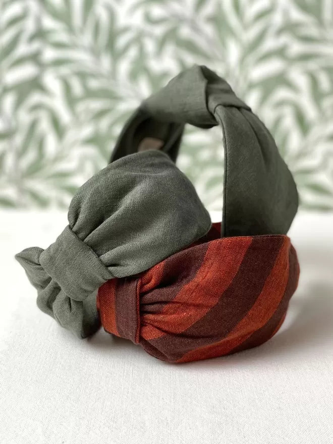Vanessa Rose Amelia Hairband in Sage Green seen stacked with a patterned wallpaper behind.
