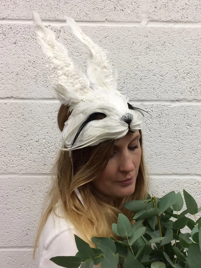 Woman wearing luxury embellished white rabbit mask atop her head as a headdress