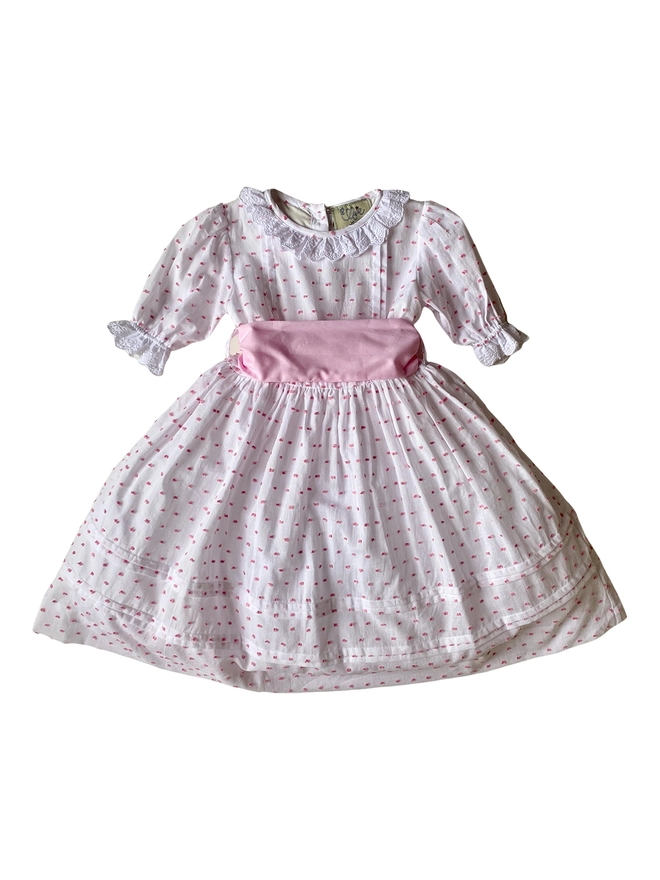 A white with pink swiss dots dress with lace edged sleeves and neckline and a pink sash