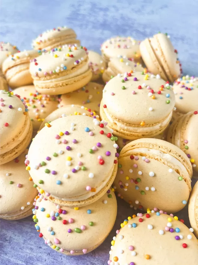 a pile of macarons with colourful sprinkles on a blue background