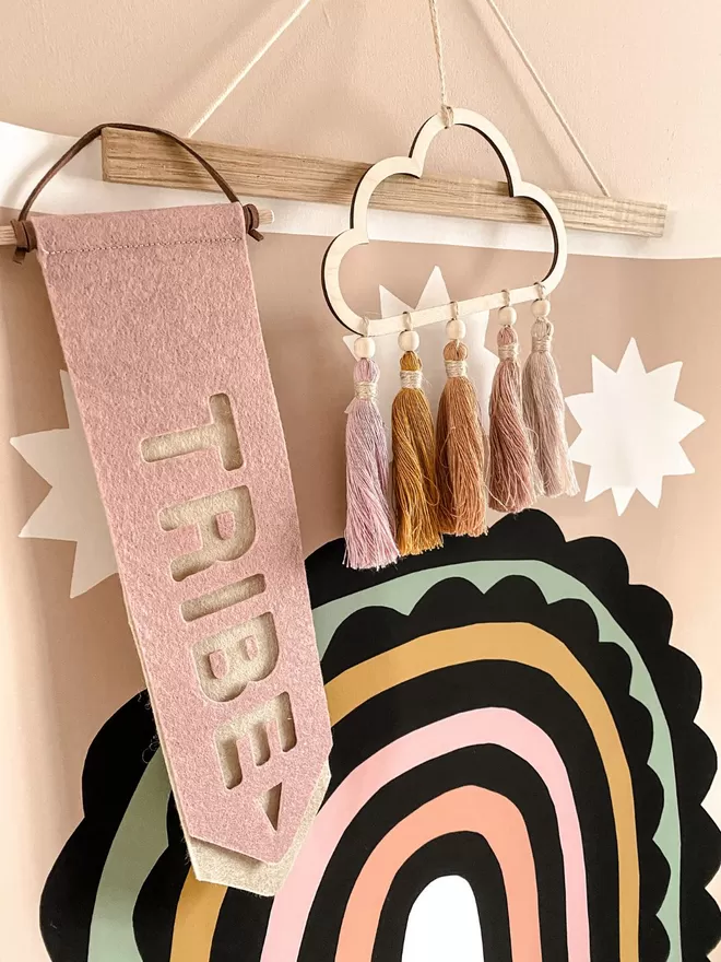 Tab Flag says tribe, hanging next to a print with a rainbow on and a wooden cloud with colourful tassels.