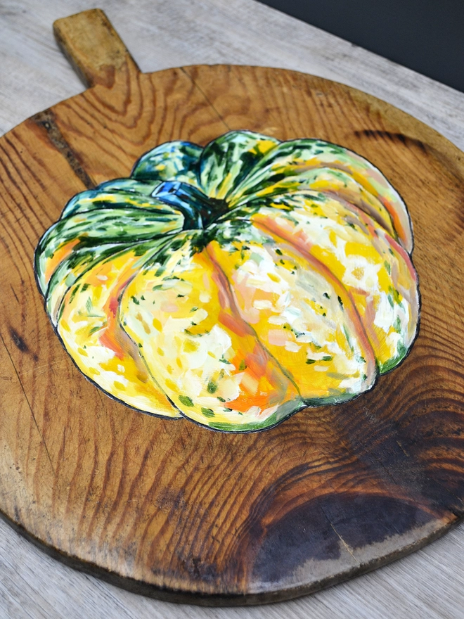 Close up of a wooden chopping board with carnival squash painted design lying on a table