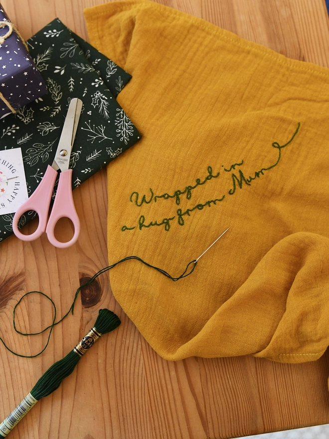 A piece of mustard yellow cotton fabric is being embroidered with a special message,