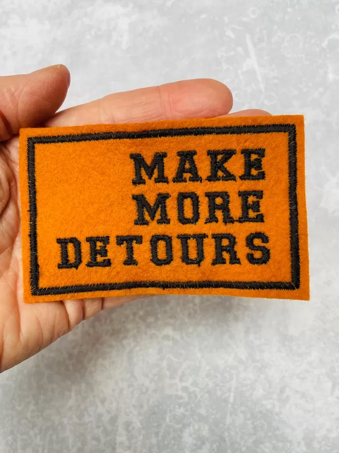 Make more detours patch being held in a hand to show scale.