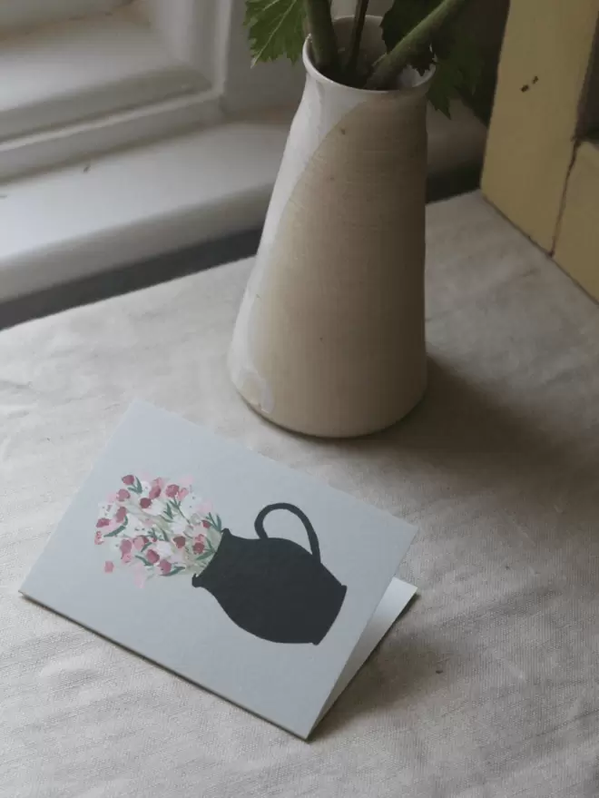 mini greetings card with vase of flowers on, on linen tablecloth
