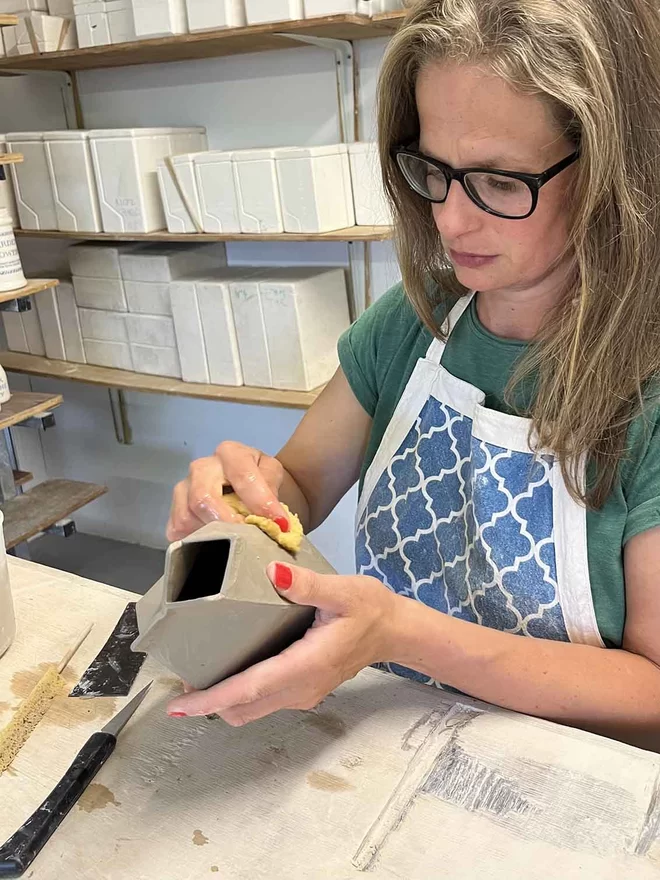 Katie Brinsley at her work bench holding a freshly made clay milk carton.