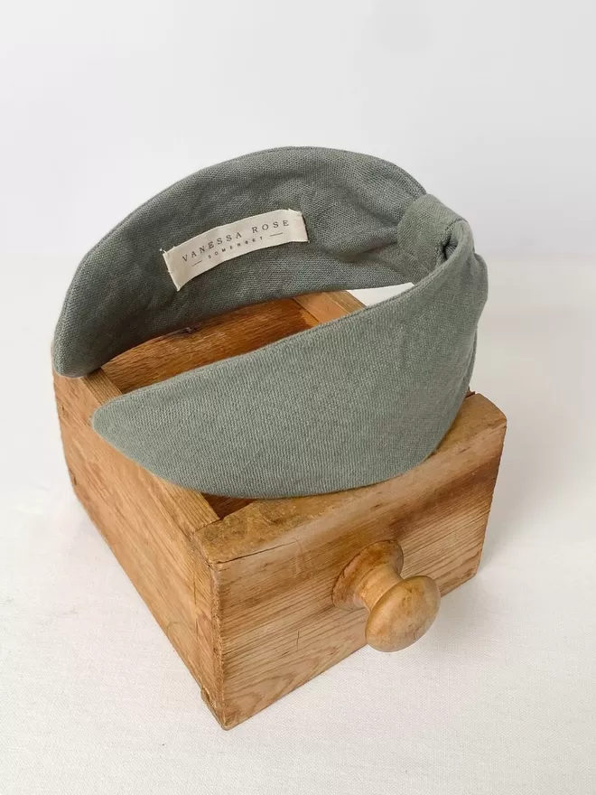 Vanessa Rose Ines Headband in Sage Green seen on a wooden store.