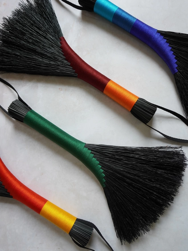 Four black broomcorn handbrooms in a variety of bright colours