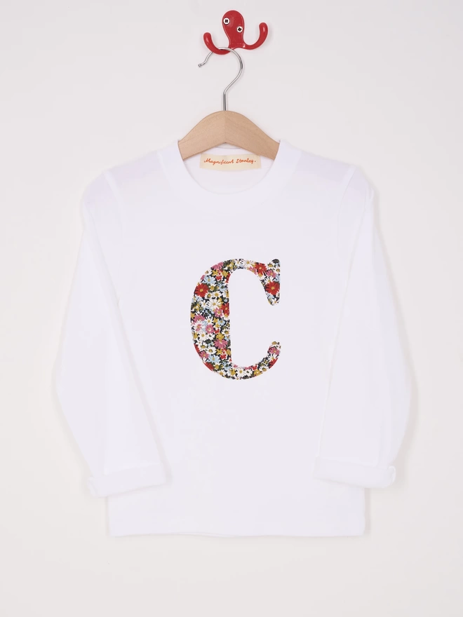 A white cotton long sleeve t-shirt appliquéd with an initial in a floral Liberty print, hanging on a hanger