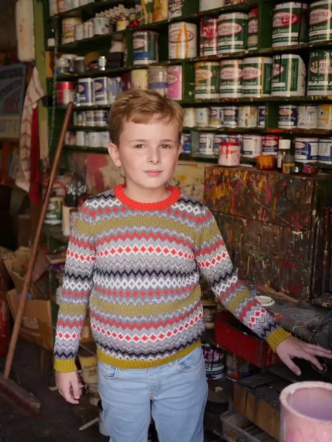 A young boy wearing 'The Daydreamer' Knitted Jumper by The Faraway Gang and holding an umbrella above their head in a paint shop.